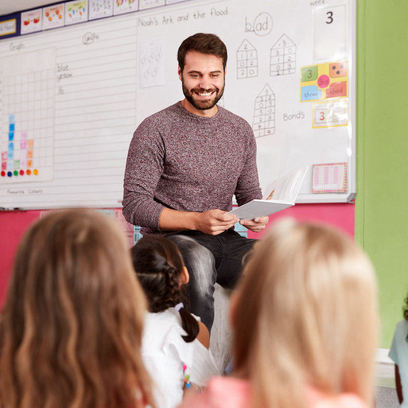 Male teacher smiling while sitting on a table teaching his class