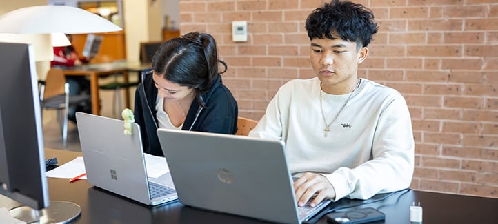 A male and female students using their laptops in a library