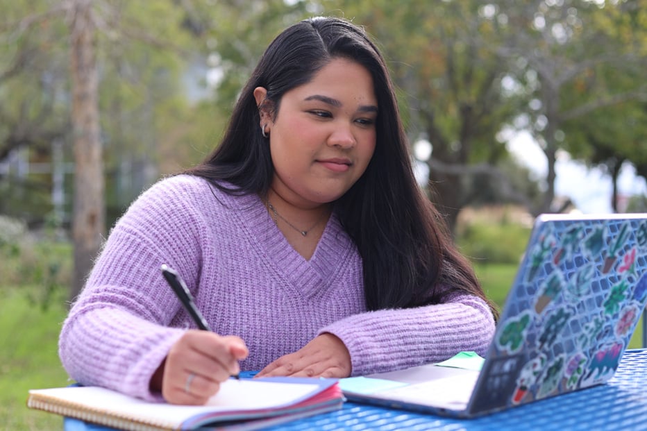 Female student studying with her laptop and taking notes on notebook