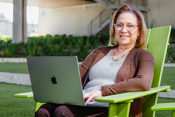 Brenda an online student at the Alamo Colleges on her laptop sitting outside on a green lawn chair