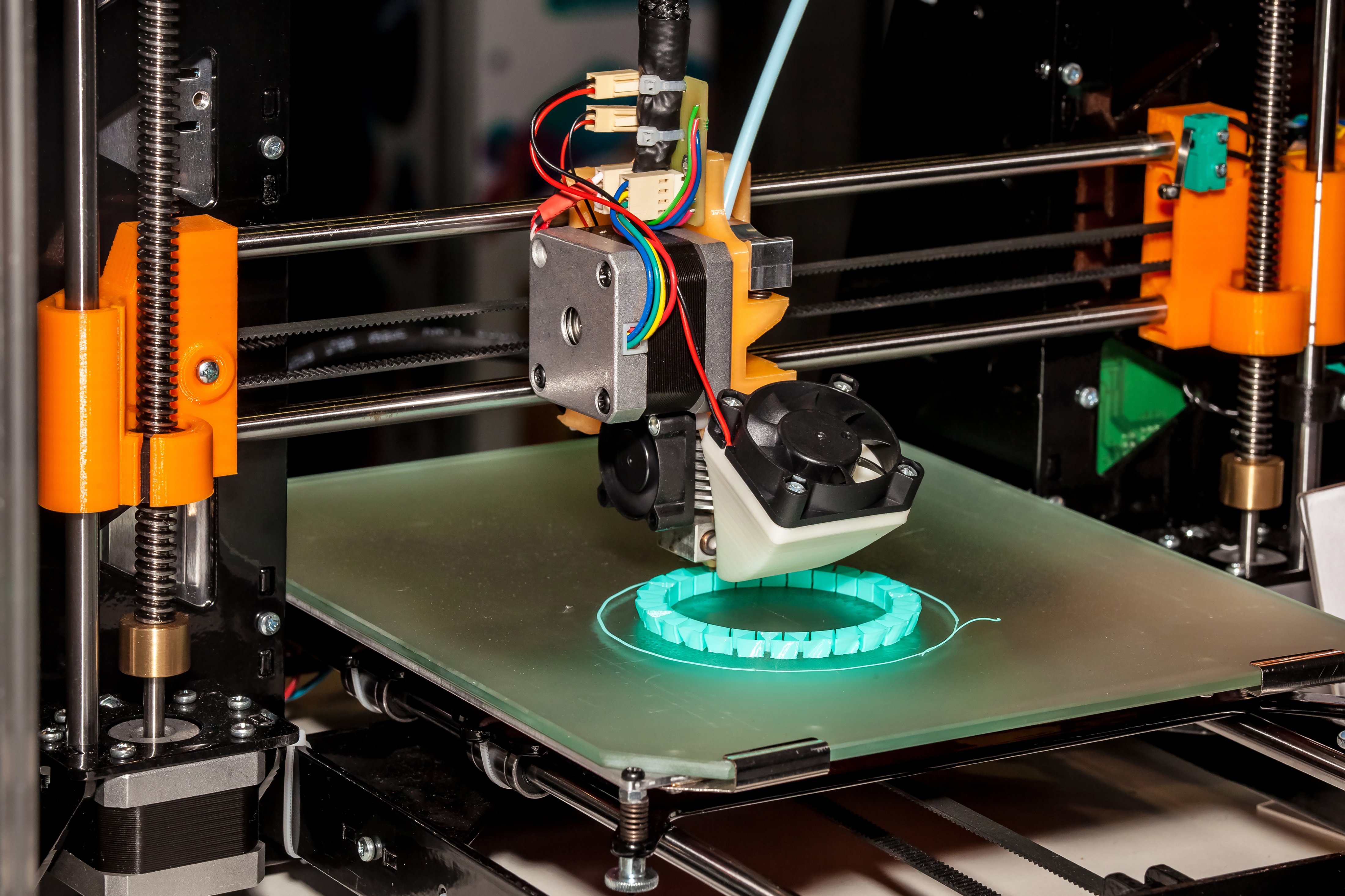 3D printer enclosed in a black cabinet, printing a white object on the build plate.