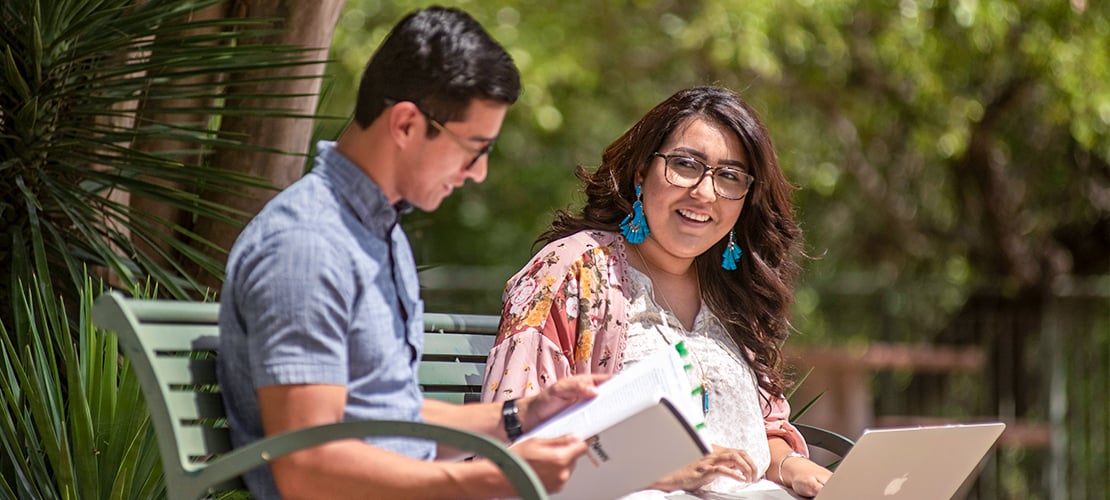 Two students studying outdoors on a bench