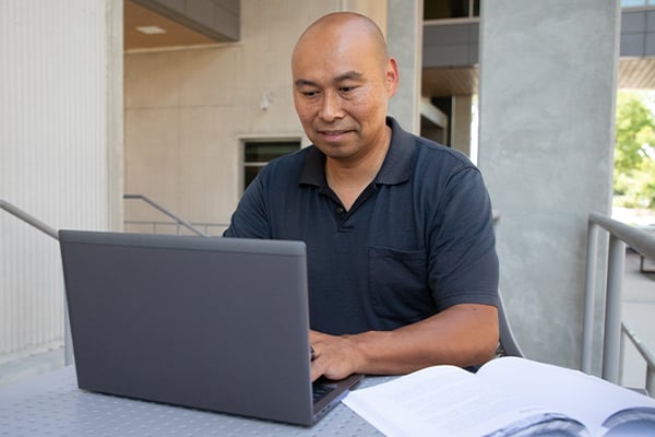 Scottie an online student at Alamo Colleges on his laptop with a textbook.