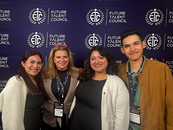 Four smiling professionals pose together at a Future Talent Council event, standing before a dark branded backdrop and conveying warmth and camaraderie.