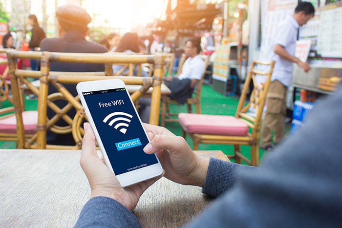 Image: Man sitting outdoors holding phone; Phone Text: Free Wifi with wifi symbol icon