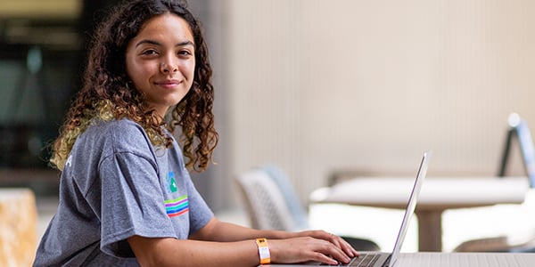 Woman wearing a grey Alamo Promise branded t-shirt while working on a laptop computer
