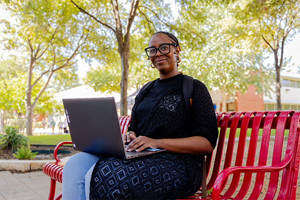 Alexuss an AlamoONLINE student sitting on a red beach outside