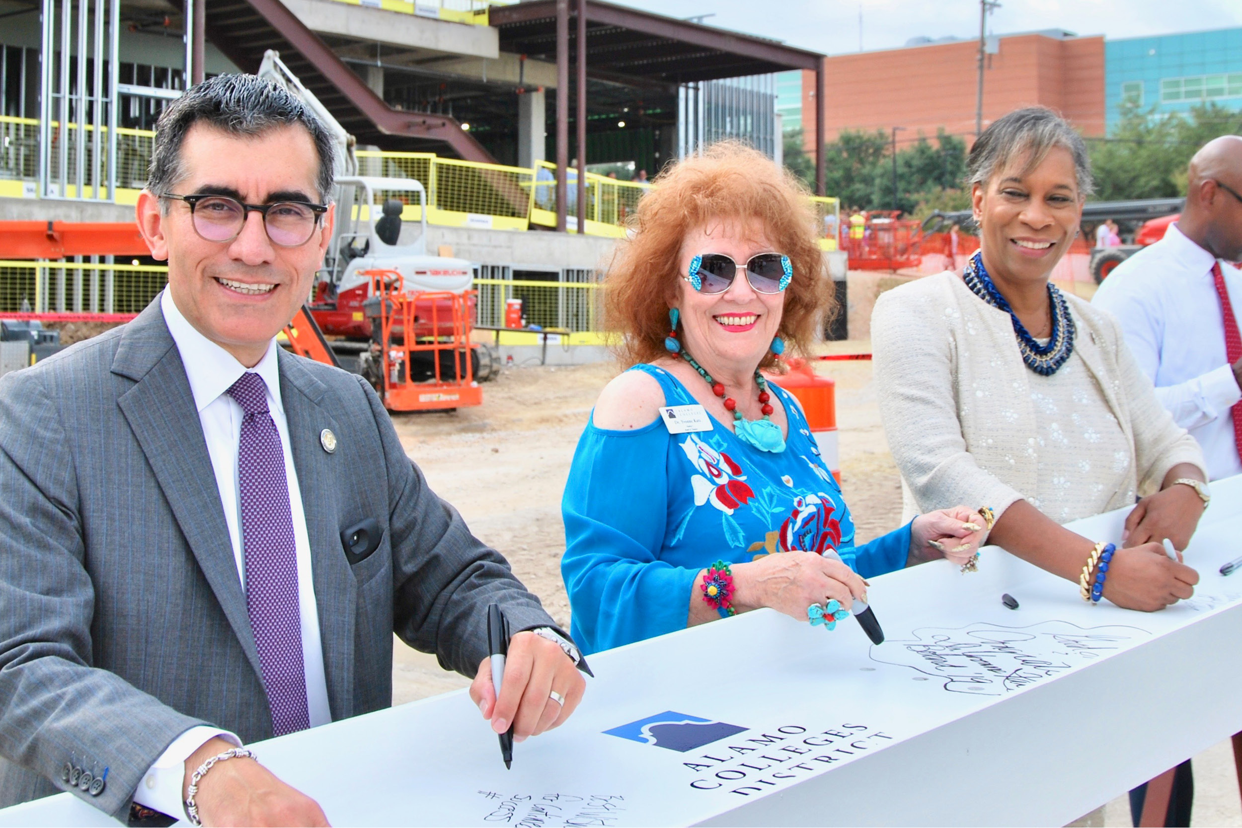 Chancellor Flores, Trustee Katz, and Dr. Loston signing a building beam outside